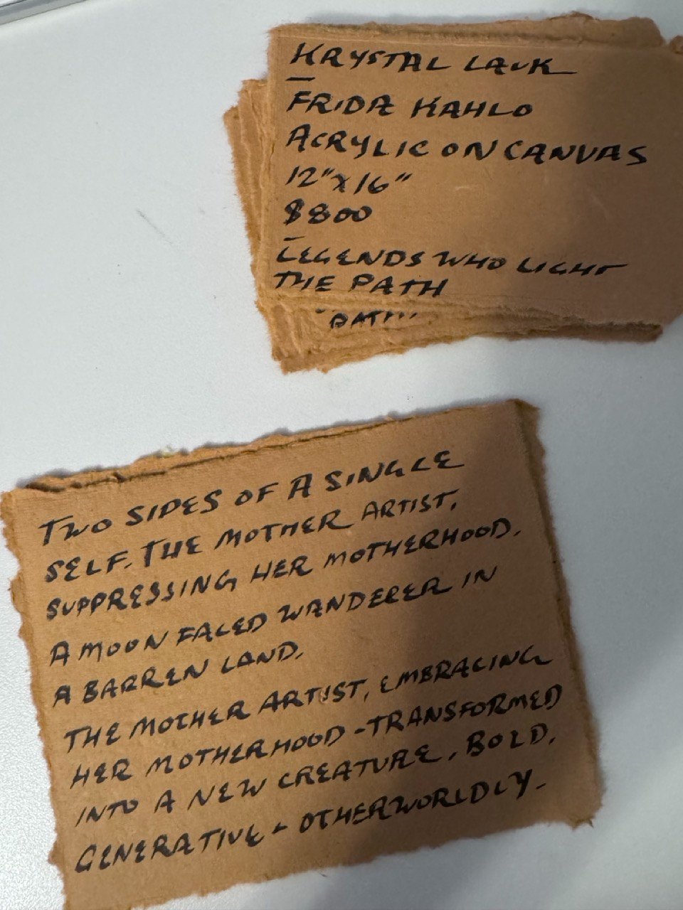 Handwritten artist cards on torn handmade paper at a Pissed Off Moms show.