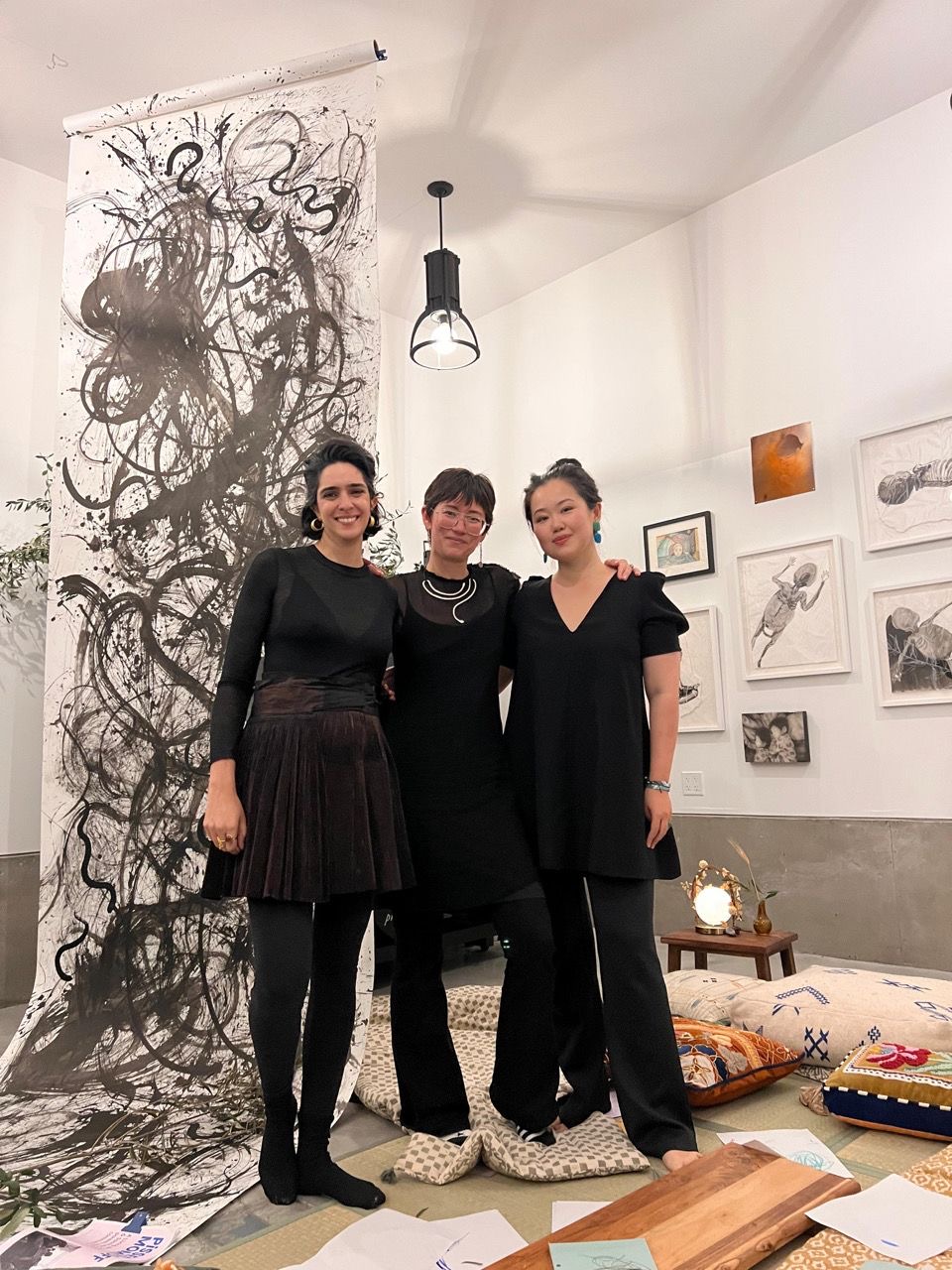 The three artists arm in arm in front of the towering ink scroll.