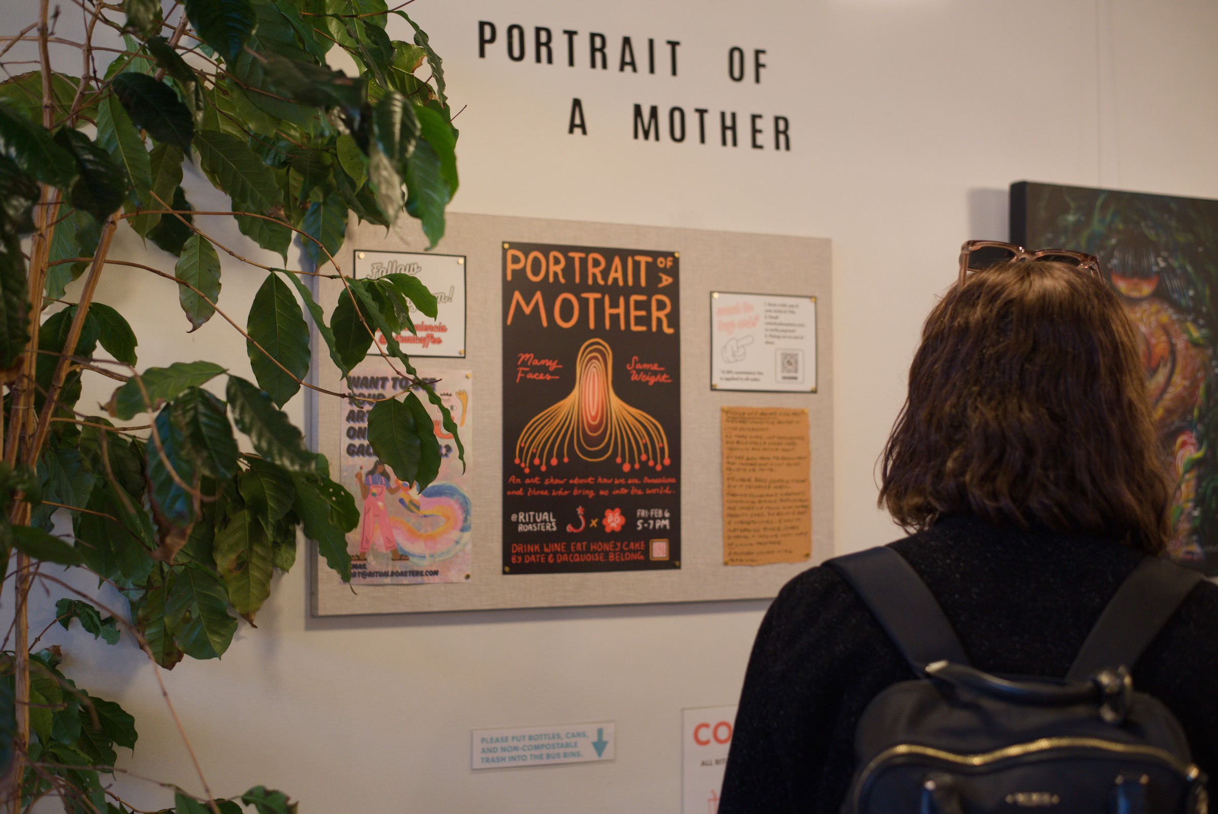 A visitor reading the 'Portrait of a Mother' show board beside a coffee plant.