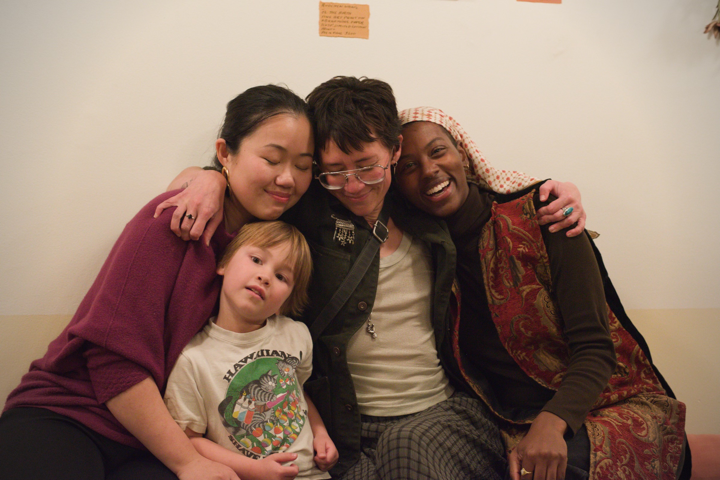 Four friends and a child in a close embrace against the gallery wall.