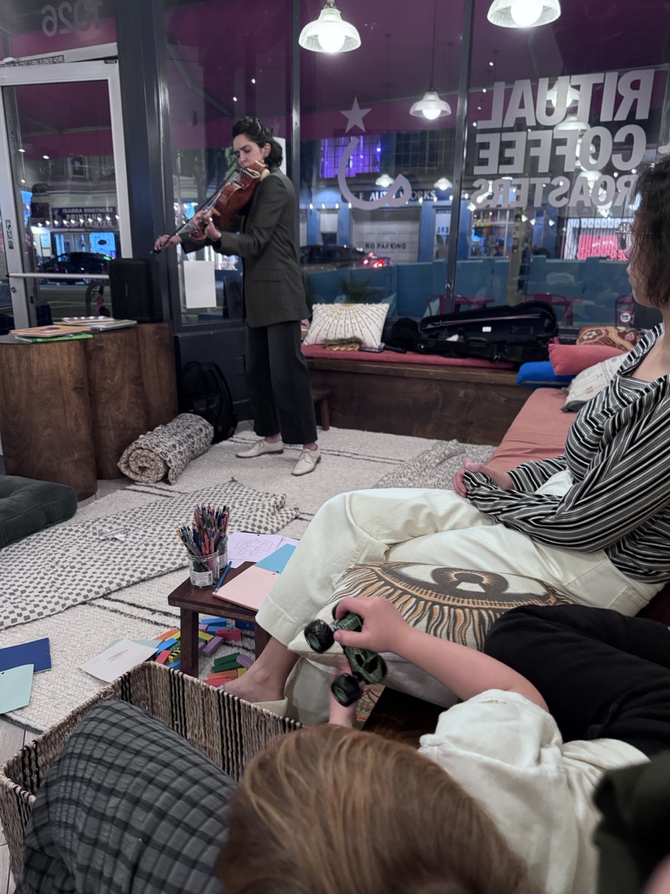 A violinist performing in the window as guests rest on cushions.