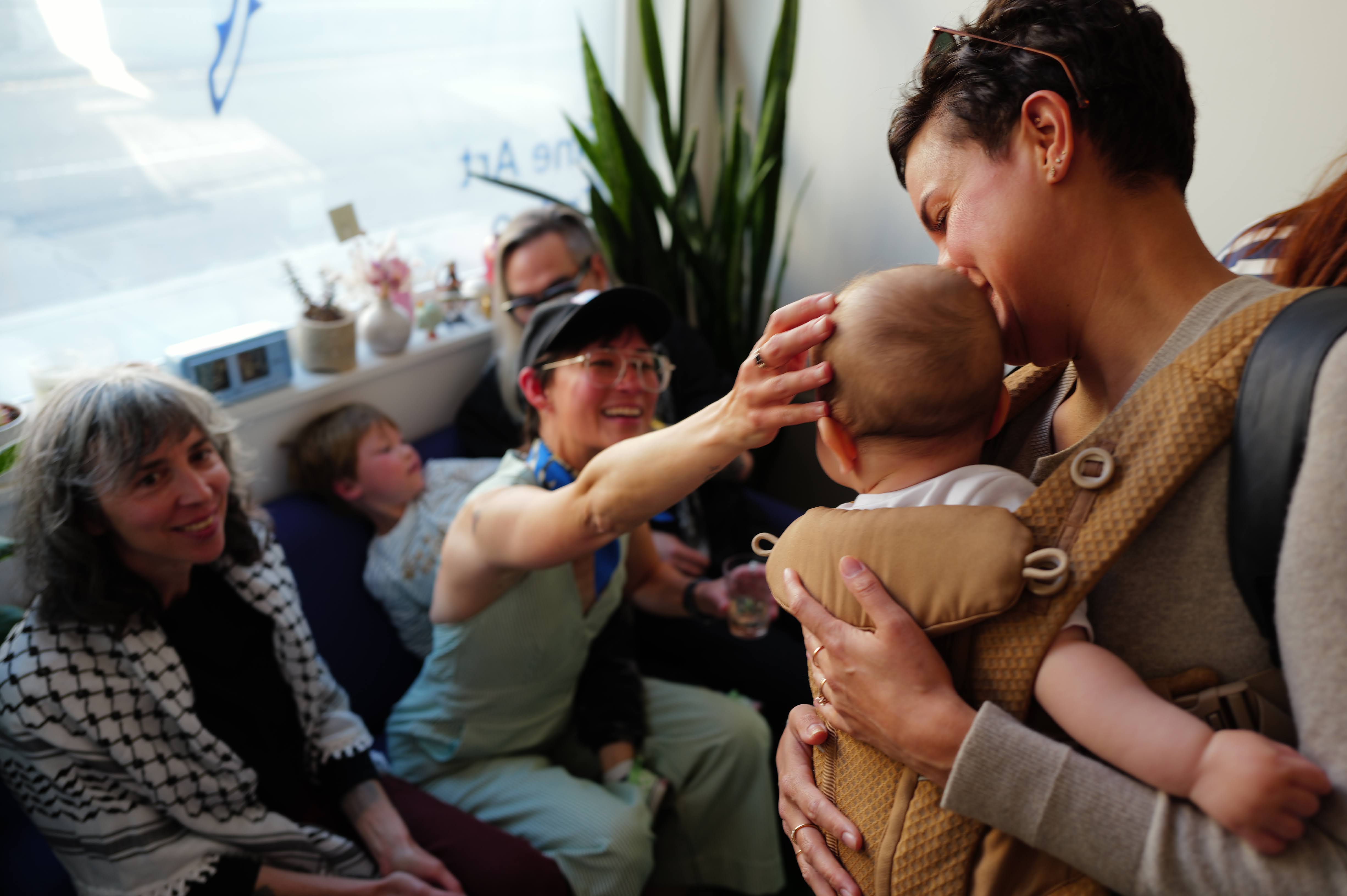 A mother kissing her child surrounded by community.