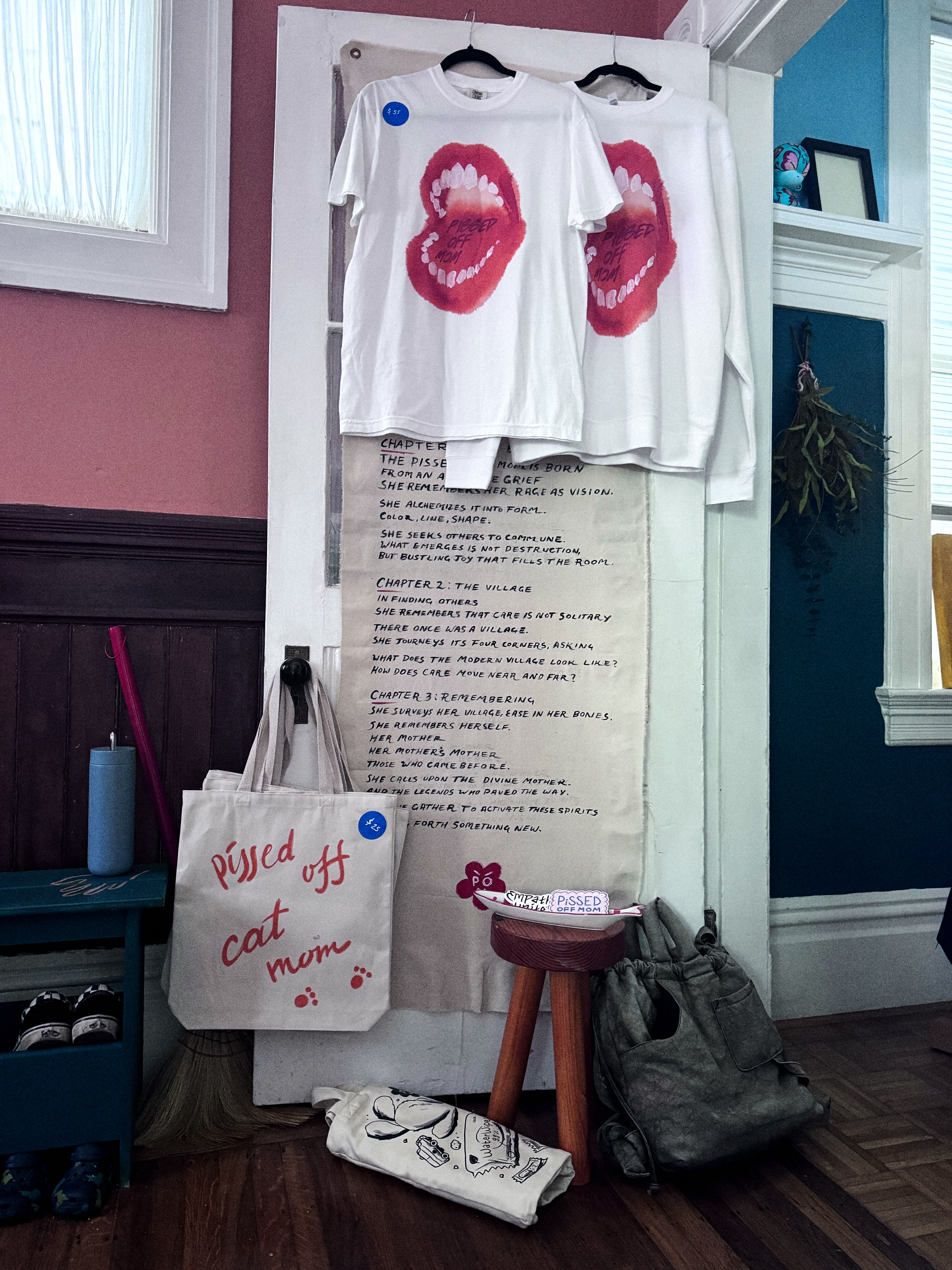 Studio shot of Pissed Off Mom merch: t-shirts, tote, zine tee, and stickers