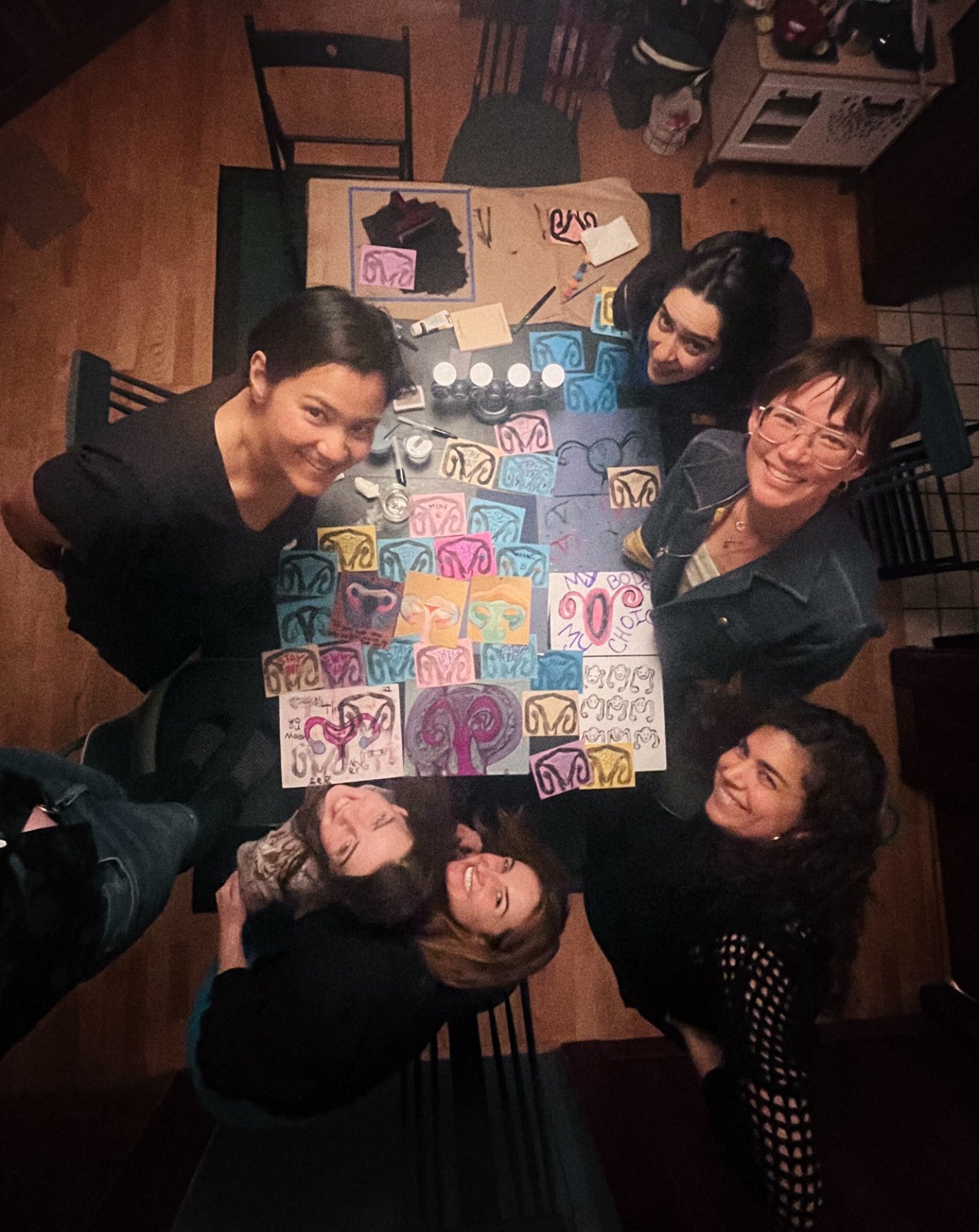 The circle gathered around the table of prints, smiling up at the camera