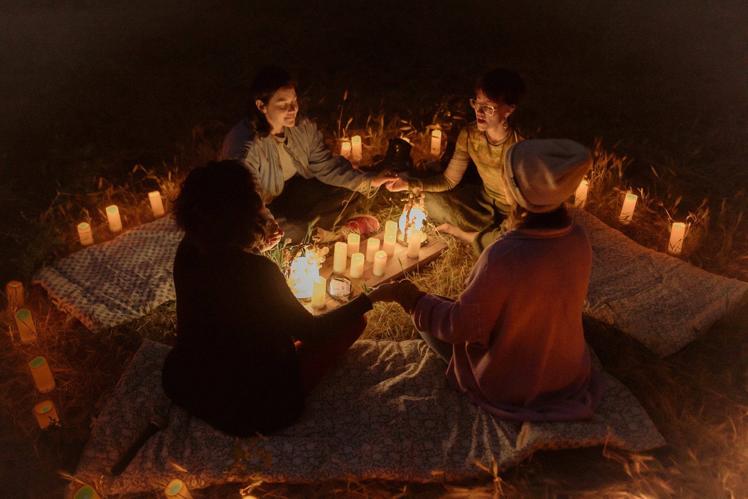 A candlelit circle of women holding hands at night.